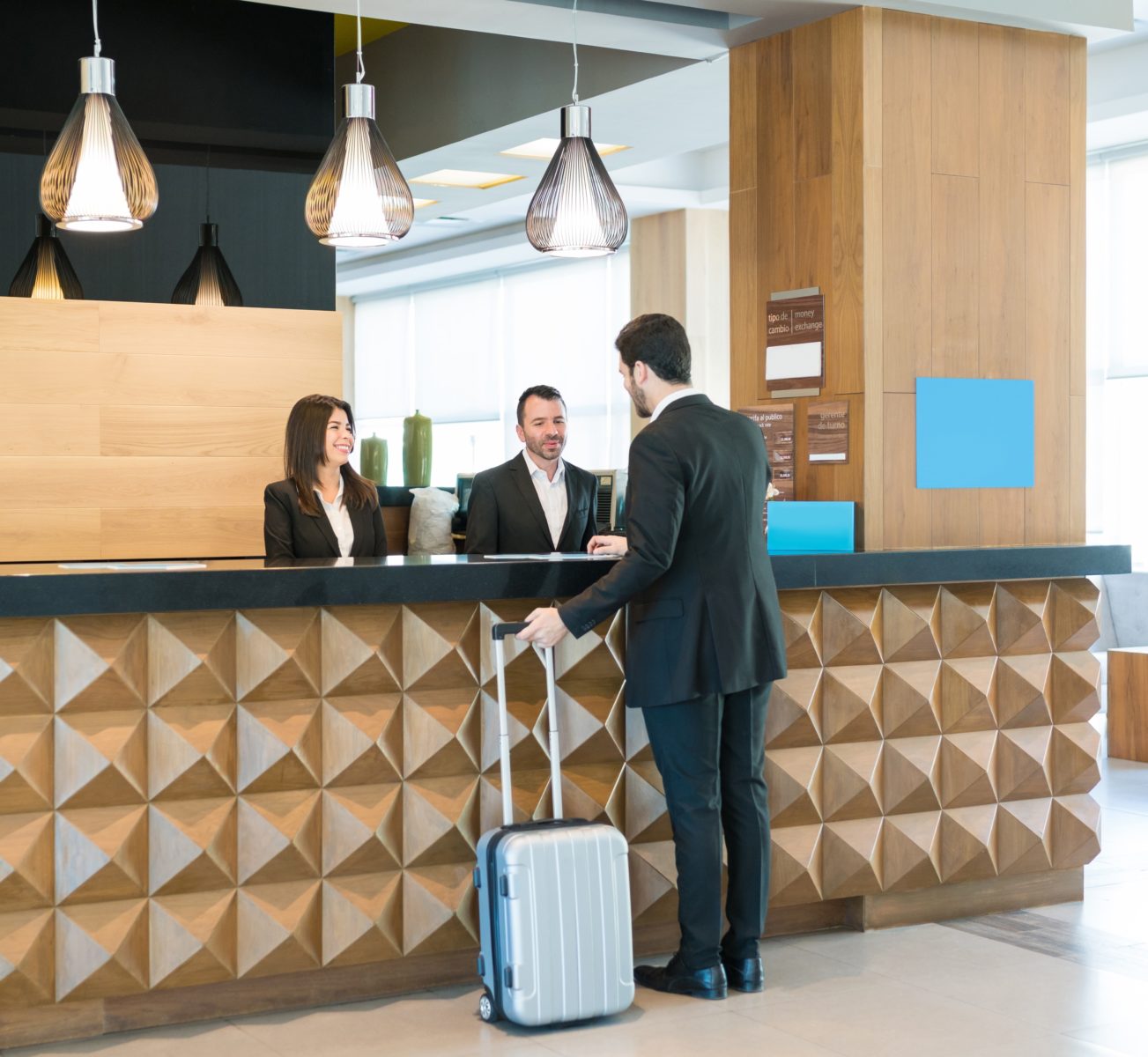 Businessman making booking at front desk with Latin receptionists in hotel lobby