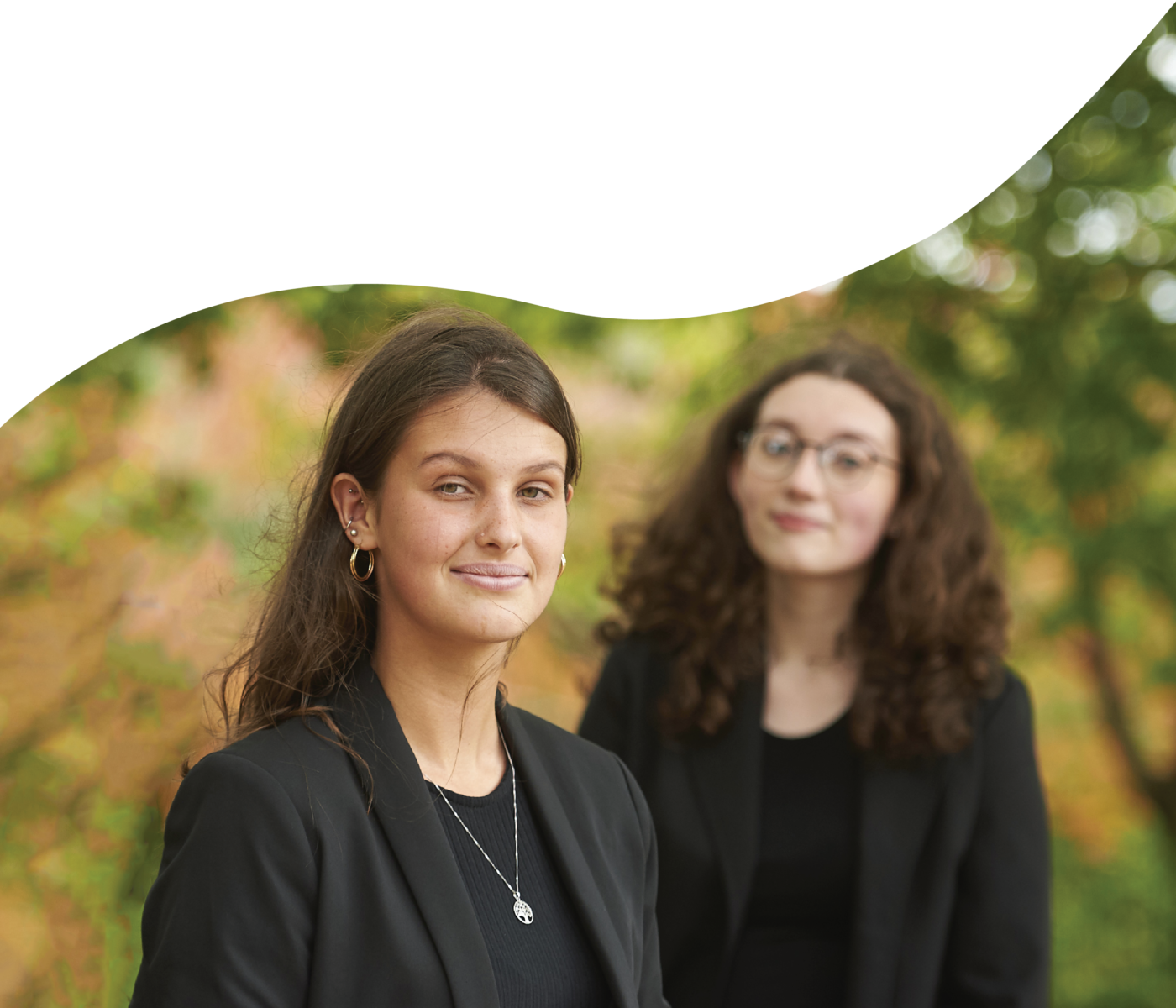 Two girls, one in the foreground and one in the background both wearing smart dress