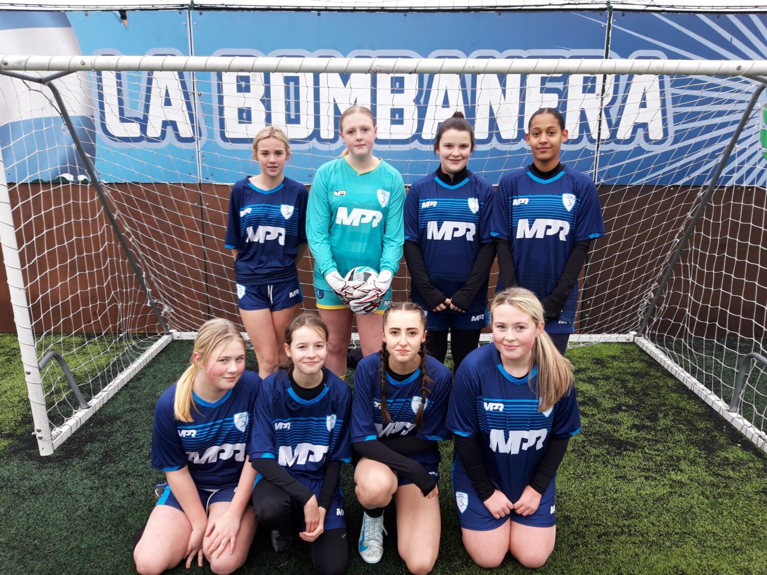 A team of girls wearing football kits smiling for a photo