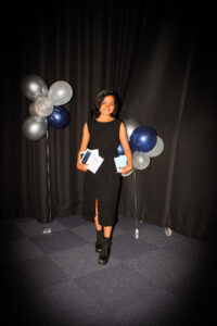 Young girl posing holding a certificate, in front of black backdrop with blue and silver balloons