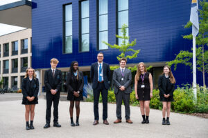 Five students and two teachers pose for a picture outside of a school