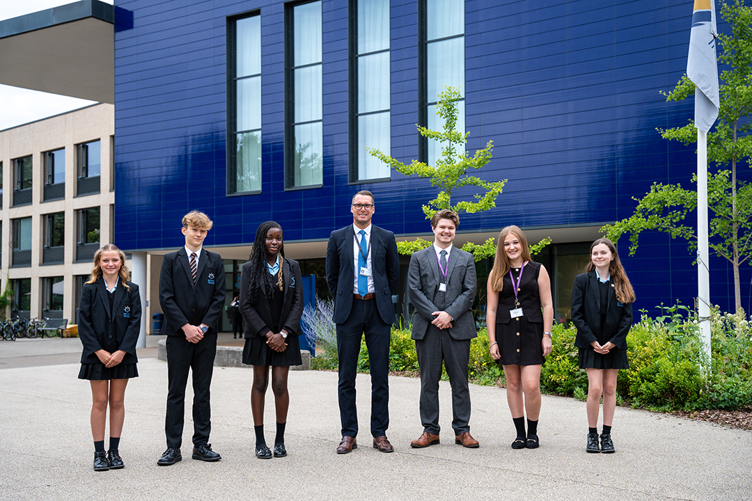 Five students and two teachers pose for a picture outside of a school